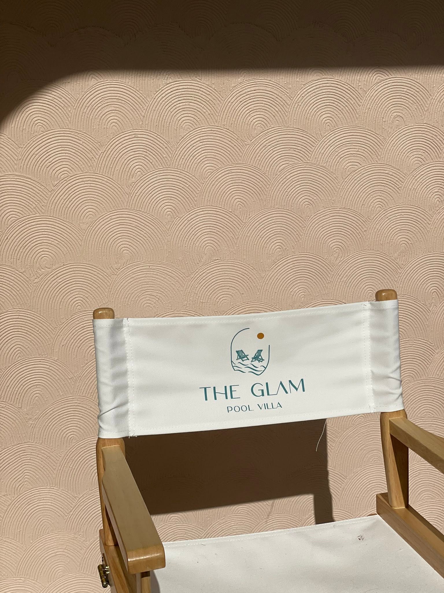 เก้าอี้ผ้าใบโลโก้ The Glam หน้าผนังปูนปั้นลายเกล็ดคลื่นสีพีช